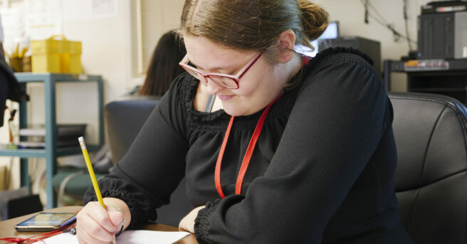 Girl with glasses sitting at a desk writing