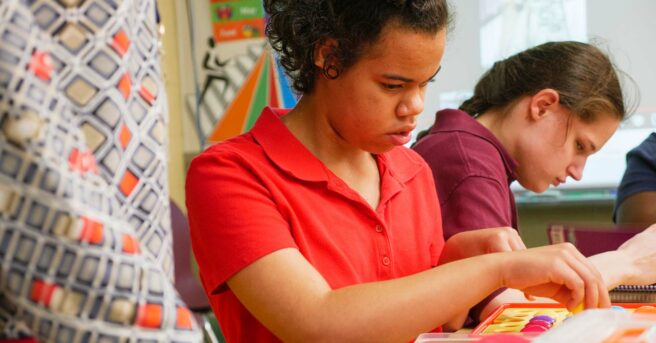 Two students working with a teacher standing next to them.