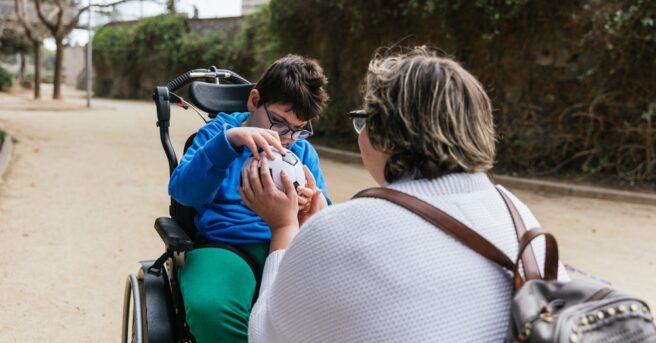child in a wheelchair explores a soccer ball with an attentive adult