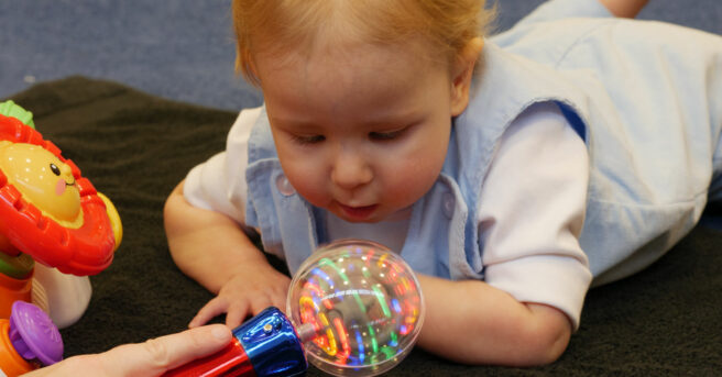 A baby on a black towel reaching and engaging with a light up toy.