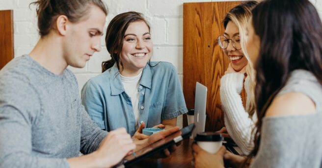 A group of 4 young people standing around a table talking.