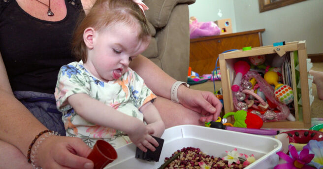 A young child playing in a sensory bin with various toys behind her