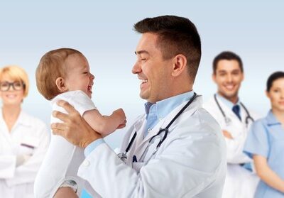 A happy pediatrician holding a baby with other medical professionals standing behind.
